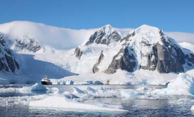 A small passenger vessel stands between icebergs with a spectacular view of the mountains of Antarctica