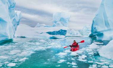 Man paddling on kayak between ice in Antractica, near Pleneau Island