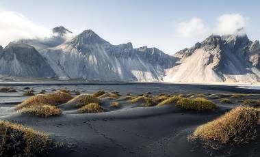 Gorgeous view on Stokksnes cape and Vestrahorn Mountain with black sand with grass on foreground at summer.