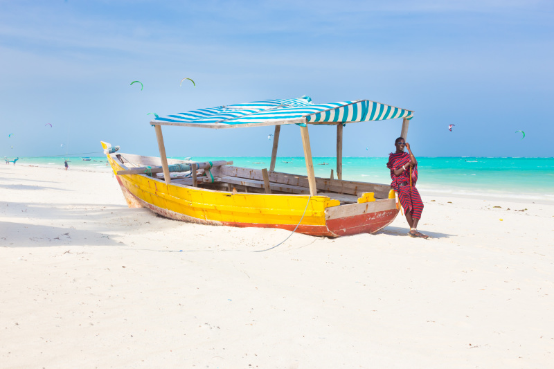 Maasai-warrior-lounging-around-on-traditional-colorful-wooden-boat-on-tropical-sandy-beach-on-Zanzibar