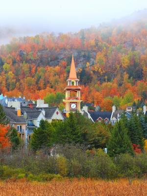 Blick auf die Kirchturmspitze des Dorfes Mont Tremblant vor der Kulisse eines nebelverhangenen Herbstwaldes