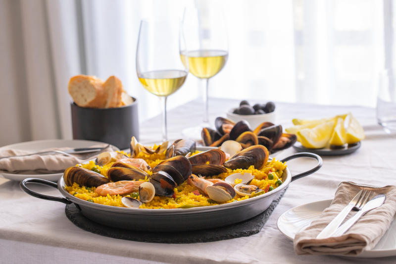 Seafood-Paella-with-prawns-clams-mussels-on-saffron-rice-and-vegetables-and-bottle-of-white-wine-on-restaurant-table