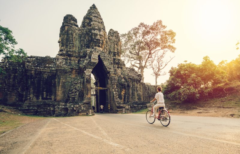 Young-woman-traveling-in-Cambodia-visiting-the-temples-of-Angkor-wat-complex-by-bicycle